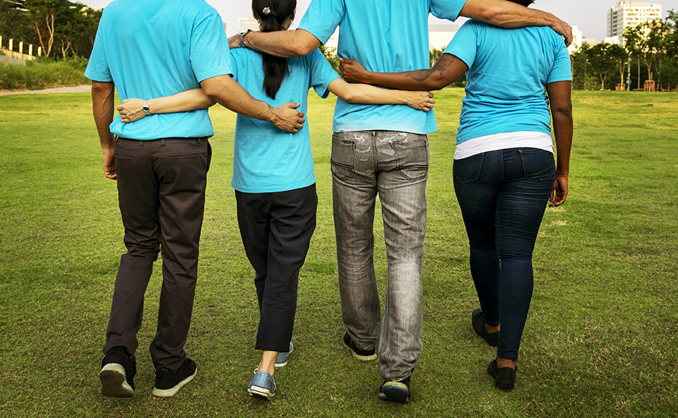 Four people in blue shirts walking with their arms on each other's backs