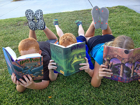 Three kids sitting in the grass and reading Harry Potter