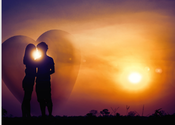 Romantic Couple standing in front of a heart with the sun shining.