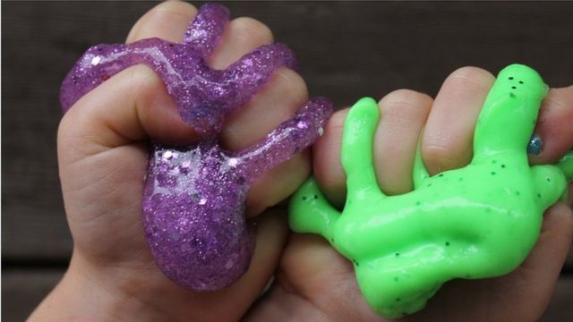 Two small hands squishing a purple and green slime between their fingers