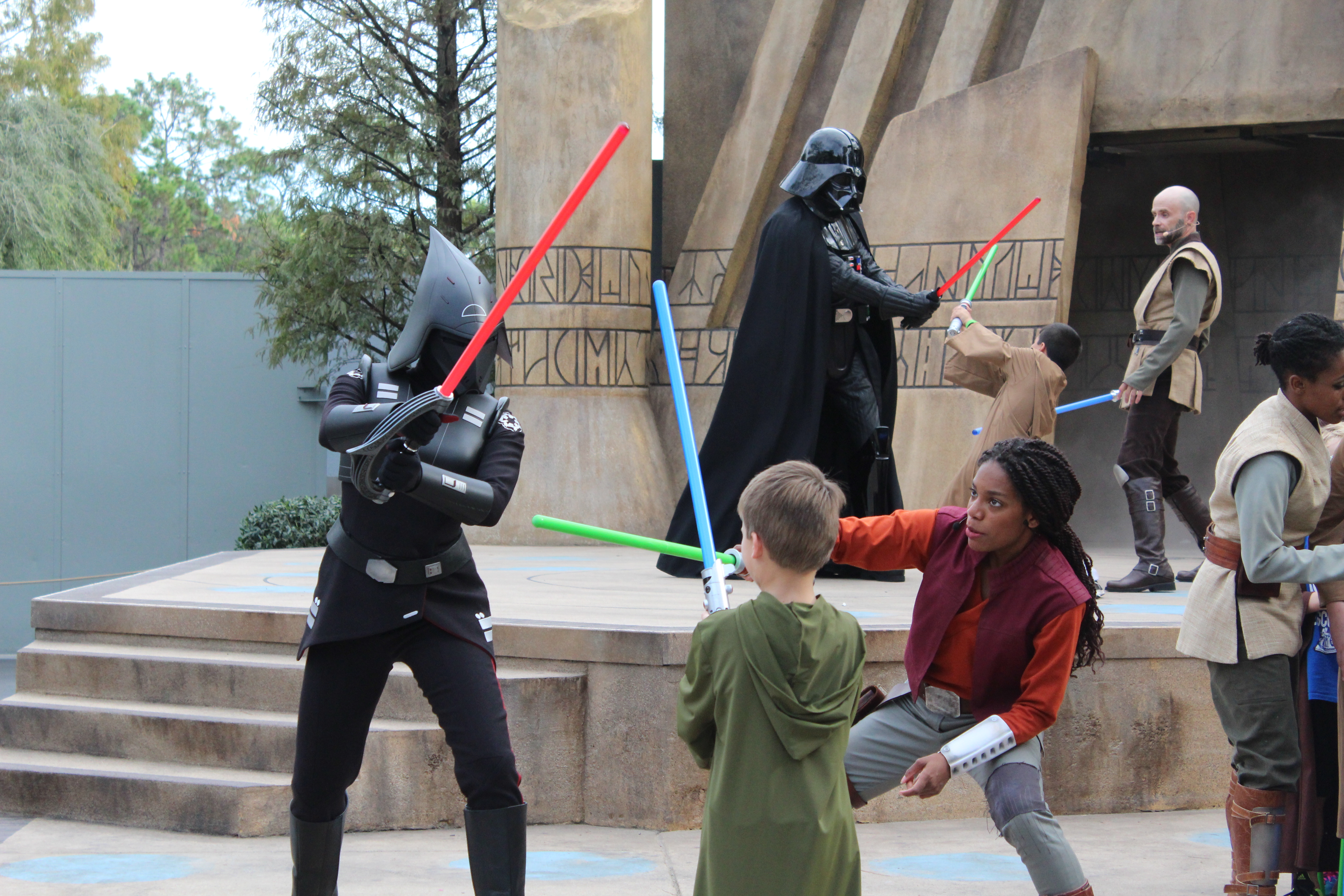 Two actors in costume teaching a child how to use a lightsaber