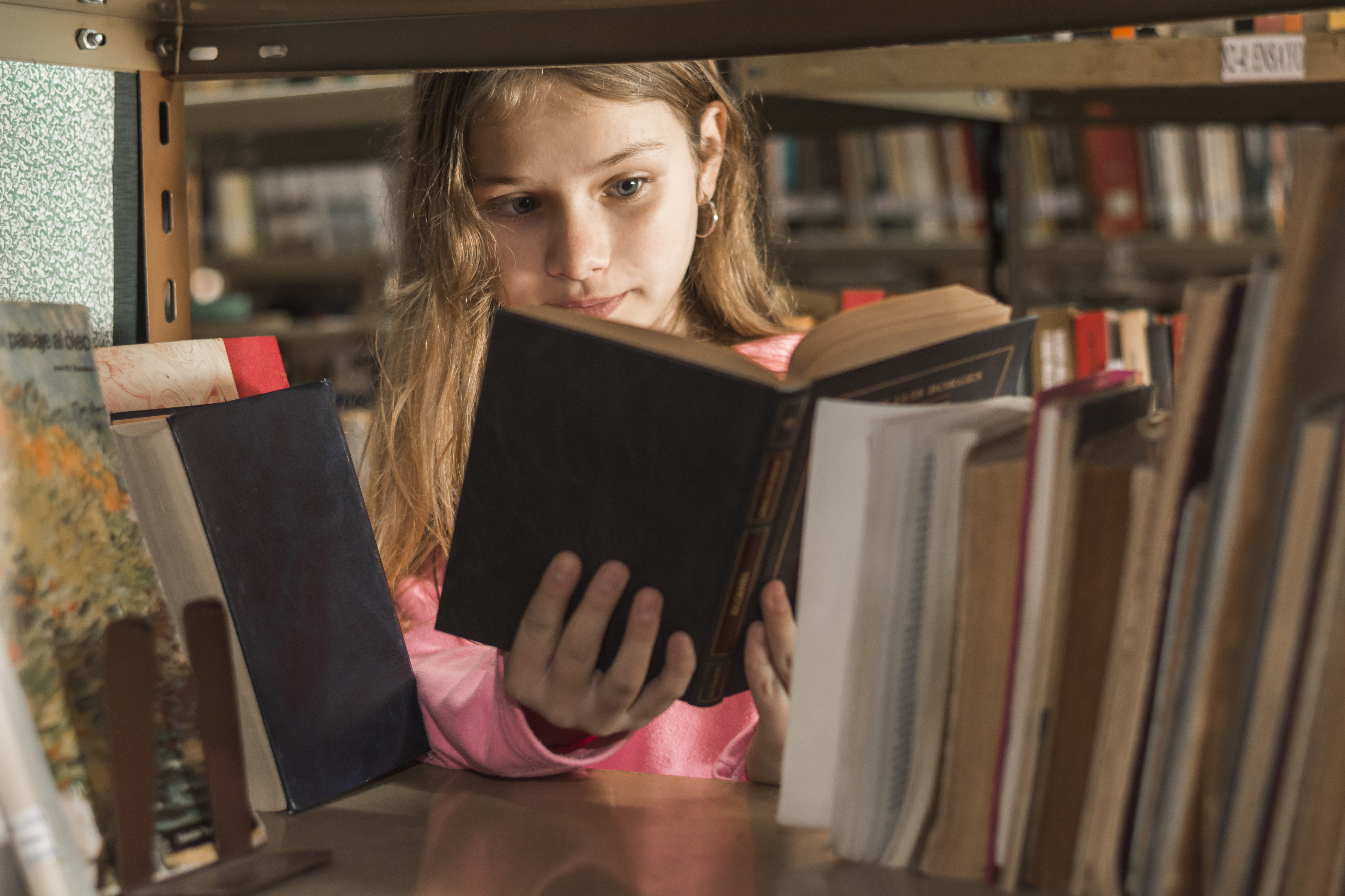 girl reading book behind bookshelf