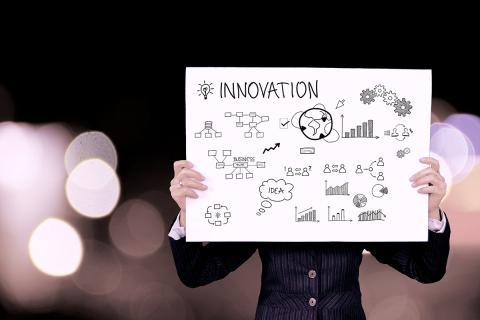 Woman in business attire holding a poster with the word "innovation" and little symbols 