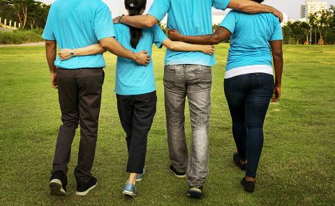 Four people in blue shirts walking with their arms on each other's backs