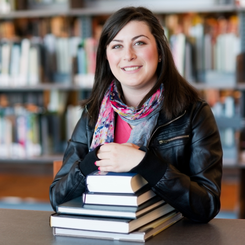 Woman sitting at table with stack of books in front of her.