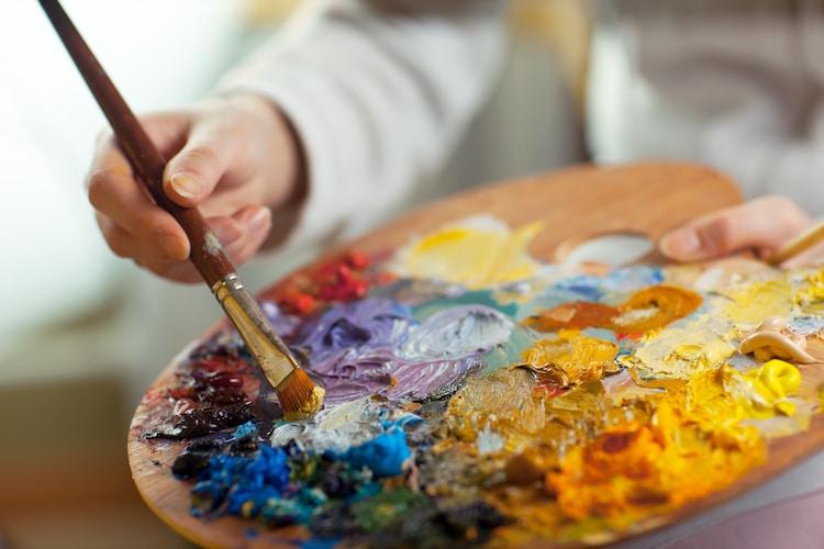 Photo of a palette of oil paints and a hand holding a paintbrush