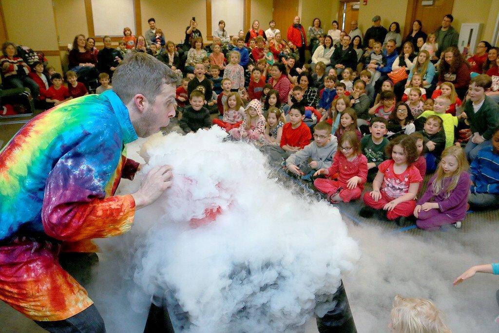 man in rainbow coat doing science in front of crowd